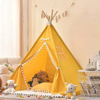 Tipi enfant intérieur jaune avec pompons, créant un coin de jeu lumineux et joyeux.